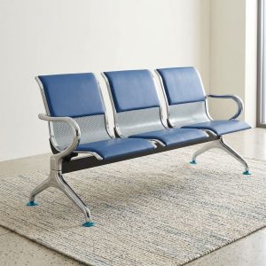 Three-seater steel waiting room bench with blue padded cushions and chrome legs in a reception area.