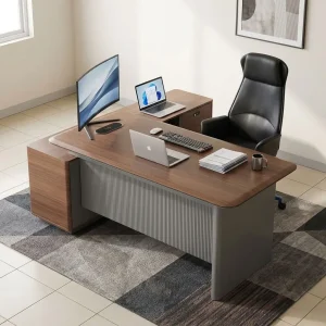 A premium L-shaped 1.6M Corporate CEO Office Desk featuring a thick teak-finished wooden top with curved corners, a prominent charcoal gray fluted front modesty panel, an integrated flip-up silver power grommet, and an attached side storage credenza with two storage drawers and open shelves.